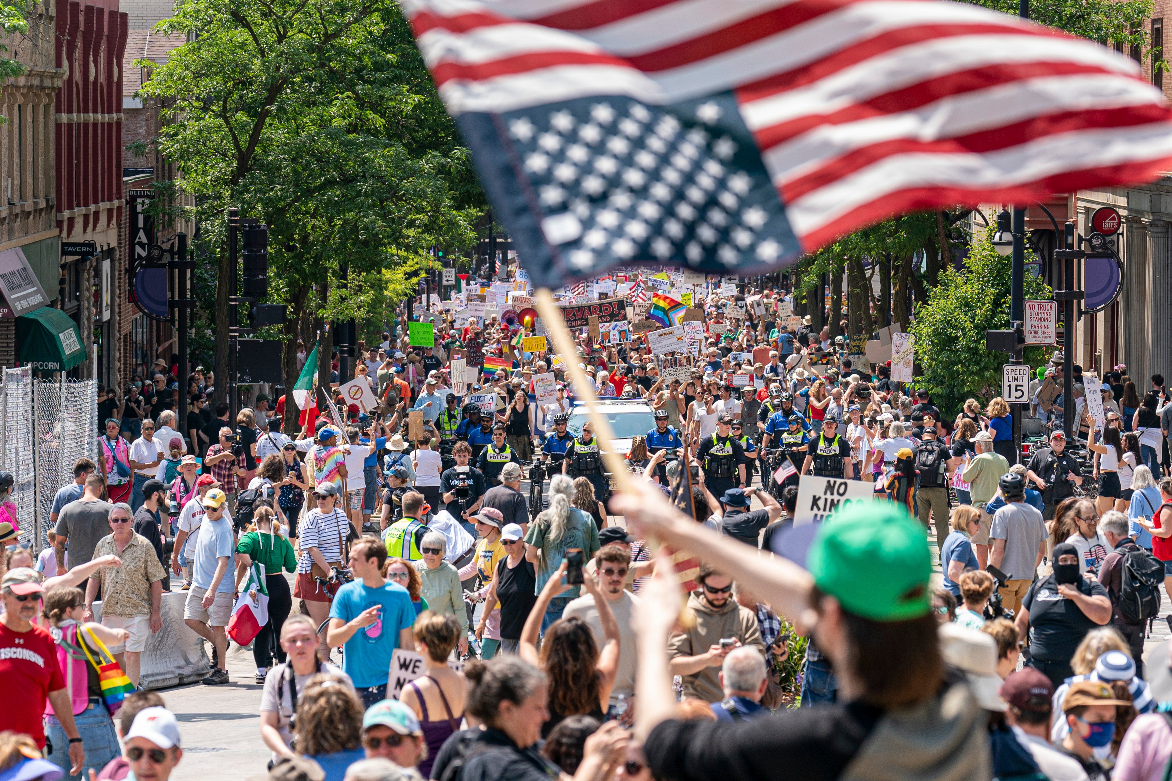 Protestor holding an American flag amidst a crowd of people on a city street.