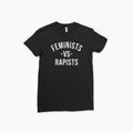 Black short-sleeve cotton t-shirt with bold white text "Feminists -vs- Rapists" centered on front.